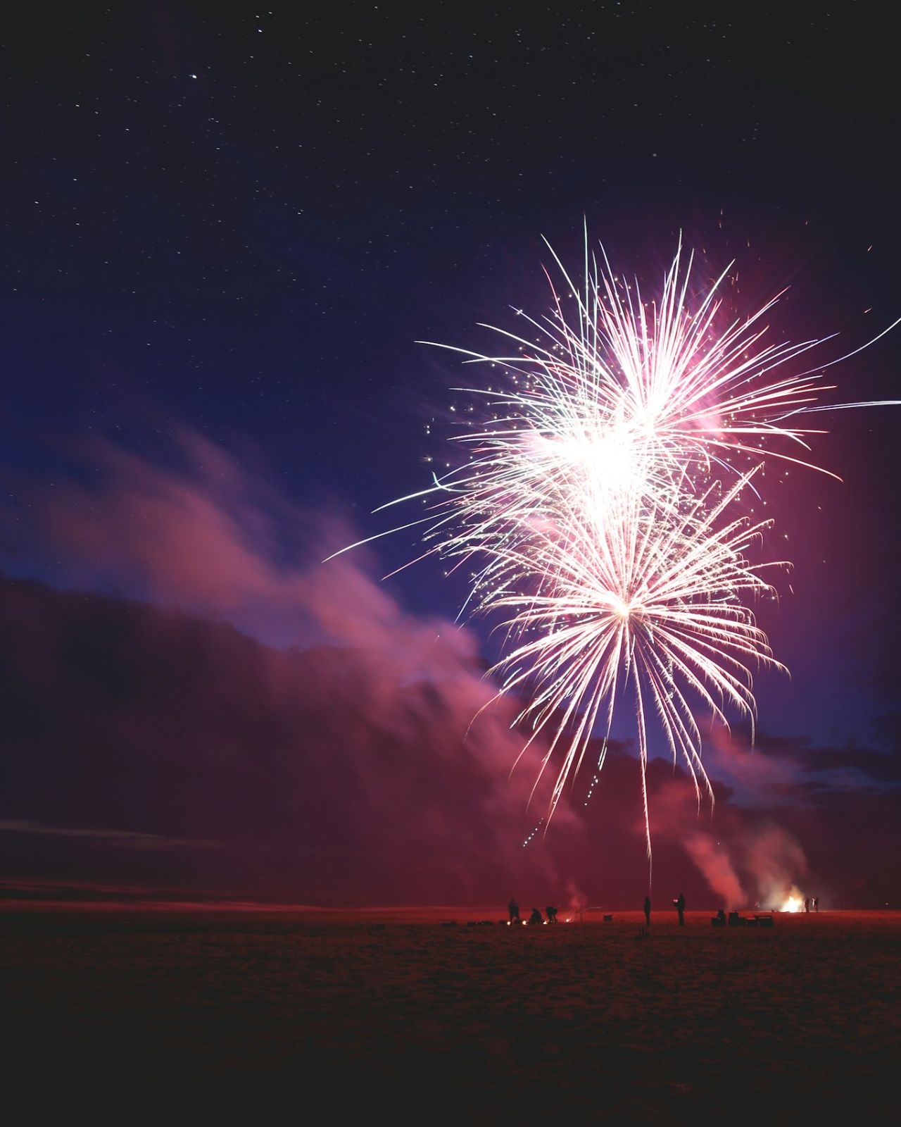 Fuochi d'artificio sopra una spiaggia di notte, con alcune persone in controluce sulla sabbia