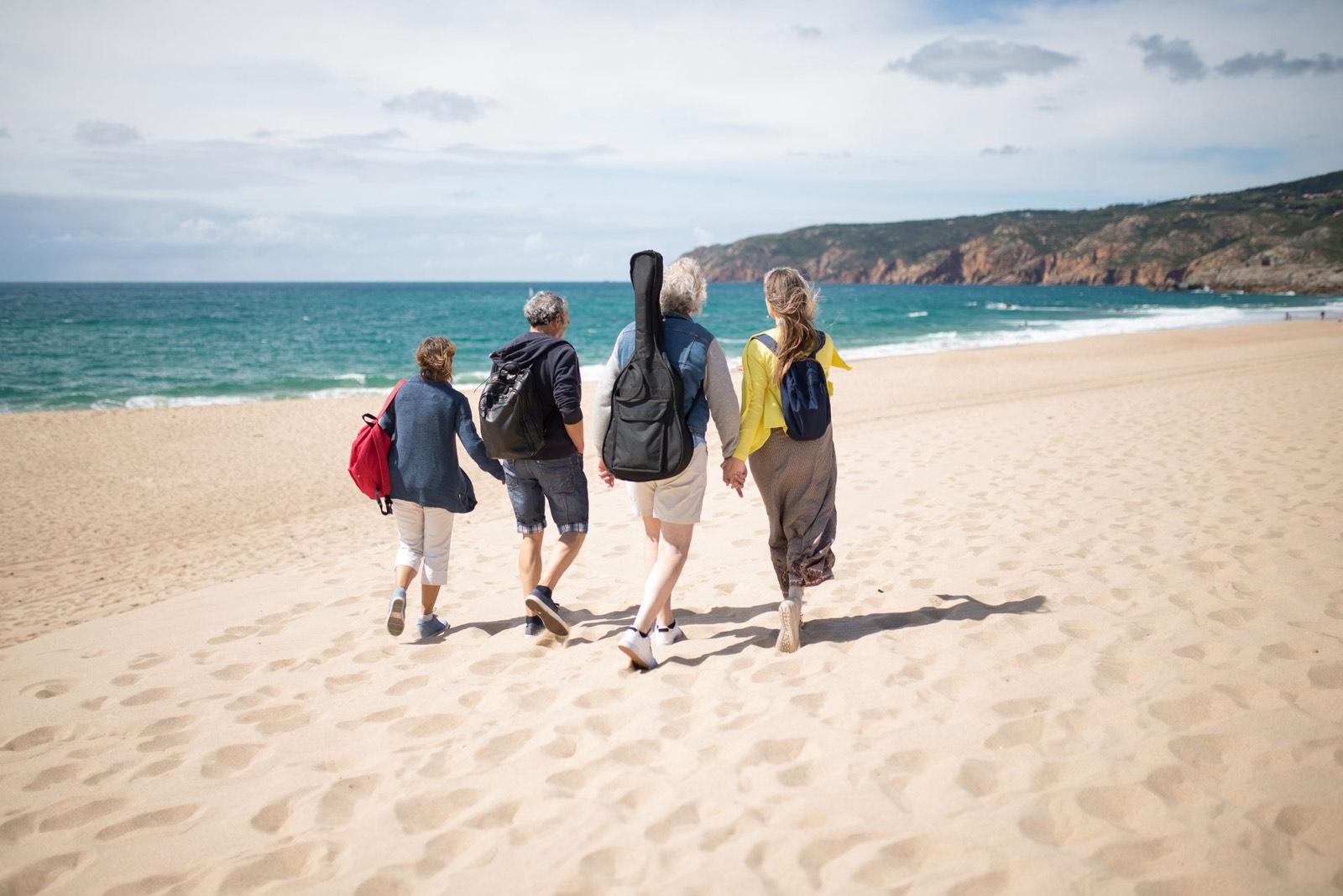 Quattro persone con lo zaino in spalla camminano insieme su una spiaggia